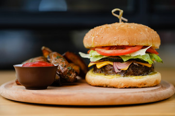 Delicious beef burger with tomato, onion, lettuce and melted cheese with sauce on the wooden table