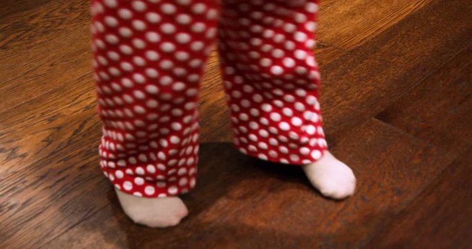 legs and feet of little child, in red trousers with white polka dots and beige socks, dancing on wooden parquet floor

