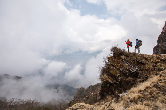 Hikers couple with backpacks relaxing on top of  mountain enjoying and make pictures view of valley above clouds