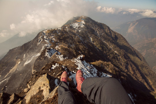 Legs of traveler hiker staying high mountain top above clouds and valley in hiking travel. Dizzy view, Freedom concept