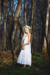 Obraz na płótnie Canvas blond woman stands in white dress by thin tree.