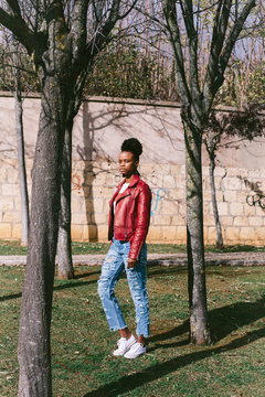 Outdoor portrait of cheerful black teenage girl wearing voluminous african hair, dressed in red Leather Jacket.