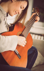 Young woman musician guitarist playing guitar at home