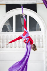 Young attractive air gymnast performs an exercise hanging on aerial silk