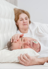 Fototapeta na wymiar an elderly woman touches forehead her husband, checking the temperature