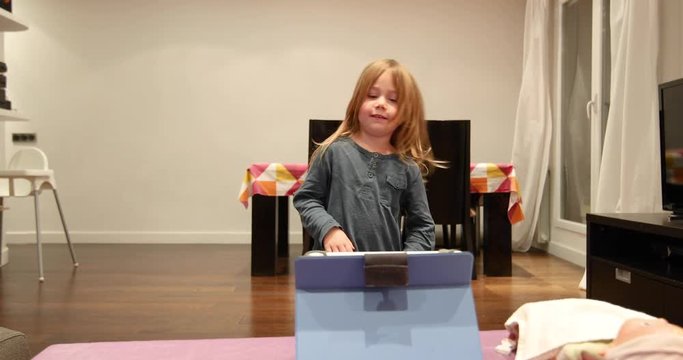 four years blonde cute child watching tablet, singing and dancing on wooden parquet floor of at living room home indoor
