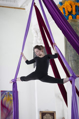 Young woman on the aerial silk performs a twine