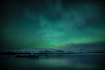 Northern lights aka Aurora Borealis glowing on the sky with mountains in Iceland © Jamo Images