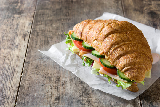 Croissant sandwich with cheese, ham and vegetables on wooden table. Copyspace