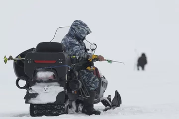 Fotobehang Man on snowmobile - fisherman on ice fishing caught fish at lake © KONSTANTIN SHISHKIN