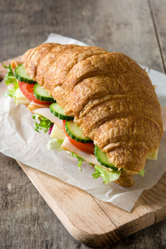 Croissant sandwich with cheese, ham and vegetables on wooden table