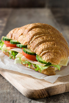 Croissant sandwich with cheese, ham and vegetables on wooden table