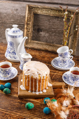 A festive tea party for Easter. A table decorated for the holiday. Homemade delicious cake in sugar icing and dyed eggs. An ancient frame for a picture in the background.