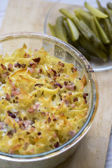 Baked meal from pasta, smoked meat and eggs called sunkofleky served with pickles
