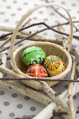 Colorful painted Easter eggs in brown wicker basket on branches, traditional Easter still life, wooden birds nest