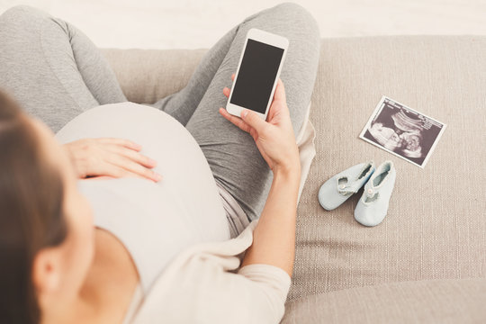Happy pregnant woman using smartphone at home