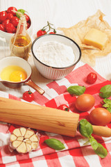 Italian cuisine  background, old kitchen tools and fresh food ingredients, Parmigiano, tomato, basil, olive oil, daugh ingredients, napkin on white rustic wooden background. Top view