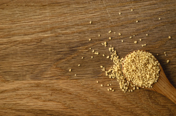 Raw Couscous Spilling from Wooden Spoon on to Oak Surface