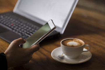 Obraz na płótnie Canvas Woman sitting at a coffee shop using smart phone and laptop