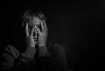 Black and white portrait image of a depressed mature woman covering her face with her hands