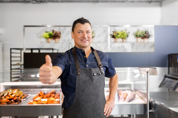 food sale, small business and people concept - male seafood seller at fish shop showing thumbs up
