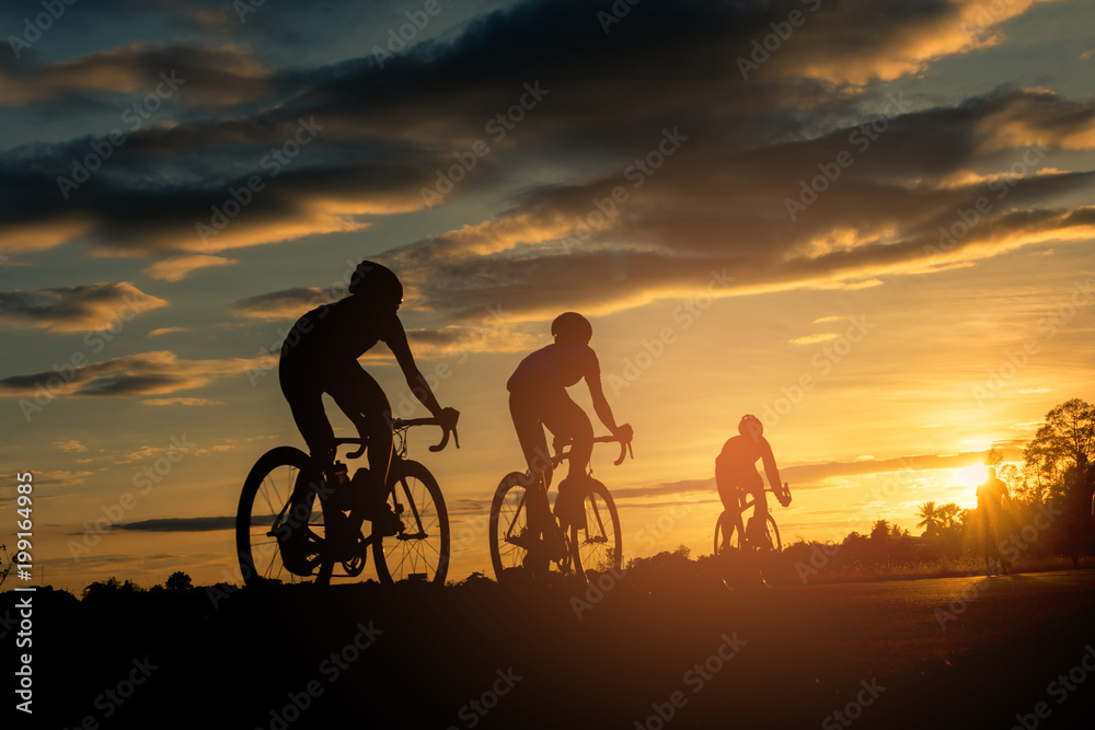 Wall mural the men ride bikes at sunset with orange-blue sky background. abstract silhouette background concept