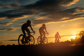The men ride  bikes at sunset with orange-blue sky background. Abstract Silhouette background...