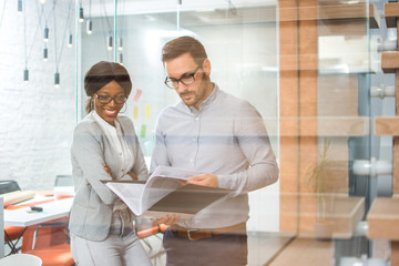 Two business people discussing documents in modern office. View through glass.