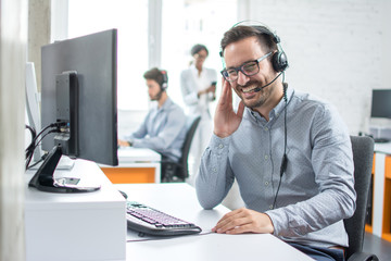 Cheerful technical support dispatcher talking with customer using headset in call center