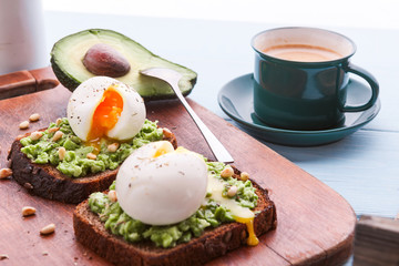 breakfast bruschetta with avocado and spinach and poached egg. with a cup of coffee