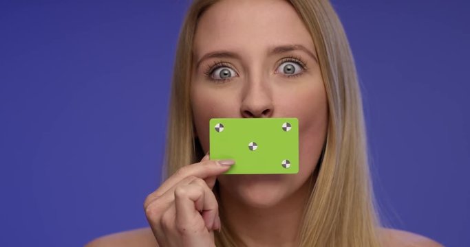 Beautiful Woman holding blank Card in front of her Mouth and looking surprised on Bluescreen