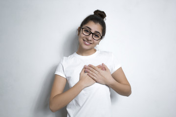 A young woman showing her cordial thanksgiving by holding her hands near the heart. The girl expresses sincere, benevolent and honest emotions. Language of the body. 