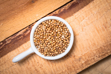 Exotic spices concept organic coriander seeds in white cup on wood background with copy space