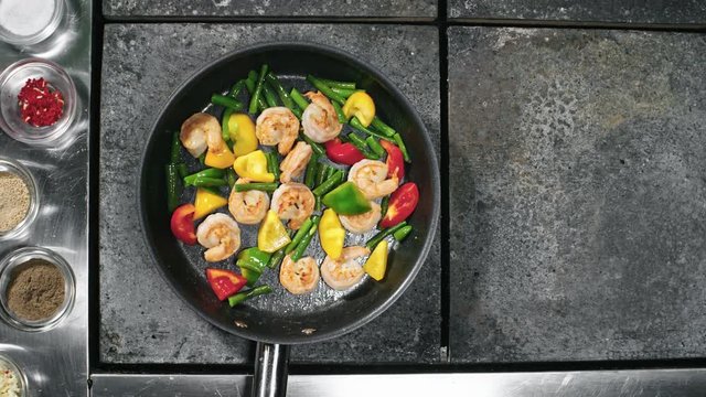 Top view of unrecognizable chef adding spices to shrimps and vegetables frying in oil, then tossing pan