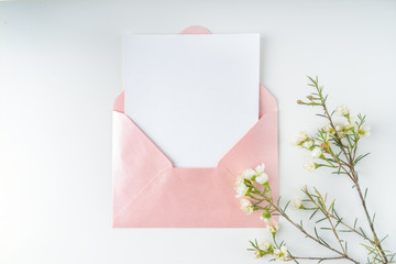 Minimal composition with a pink envelope, white blank card and a wax flower on a white background. Mockup with envelope and blank card. Flat lay. Top view.