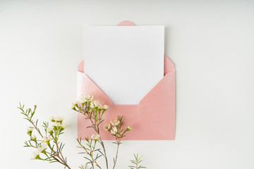 Minimal composition with a pink envelope, white blank card and a wax flower on a white background. Mockup with envelope and blank card. Flat lay. Top view. - obrazy, fototapety, plakaty