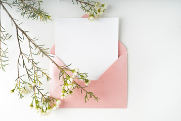 Obraz premium Minimal composition with a pink envelope, white blank card and a wax flower on a white background. Mockup with envelope and blank card. Flat lay. Top view.