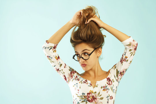 Funny pretty young woman in round glasses holding her hair up over blue background