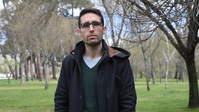 Hombre joven serio mira a c&aacute;mara y se pone unas gafas