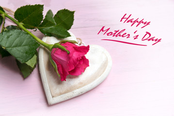 rose on a wooden heart shape on a bright pink background, text Happy Mother's Day, top view from above with copy space