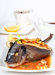 Roasted dorade stuffed with seafood on the white plate.