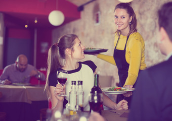 Smiling waitress bringing delicious salads to young people