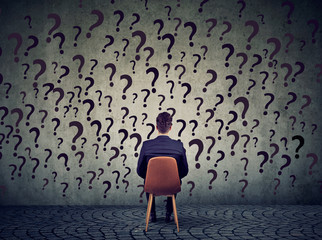 business man sitting on a chair in front of a wall has many questions, wondering what to do next