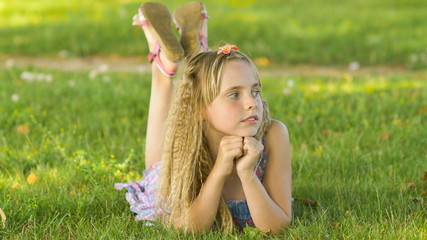 Beautiful young blonde girl lying on a field, green grass. Outdoors Enjoy Nature. Healthy Smiling...