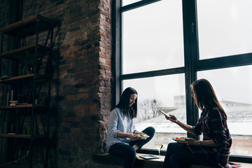 Two young women dinner sitting windowsill home