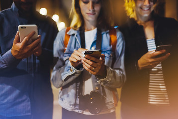Group adult hipsters friends using in hands mobile phone closeup, street online wi-fi internet concept, bloggers together pointing finger on screen smartphone on background bokeh light in night city