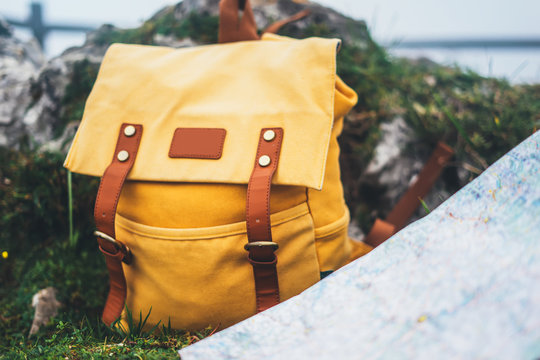 Hipster hiker tourist yellow backpack, navigation map europe on background green grass nature, blurred panoramic landscape, traveler relax holiday concept, view planning way road in trip vacation