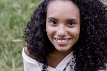 portrait outdoors of a beautiful young afro american smiling woman at sunset. Green background. Lifestyle. Nature