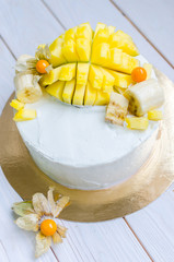 Sponge cake with white cream and a large decorative piece of mango on a white wooden table