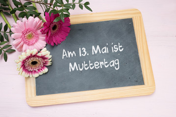 Drei rosa Gerbera Blumen auf einer Schreibtafel mit Text Am 13. Mai ist Muttertag, blick von oben